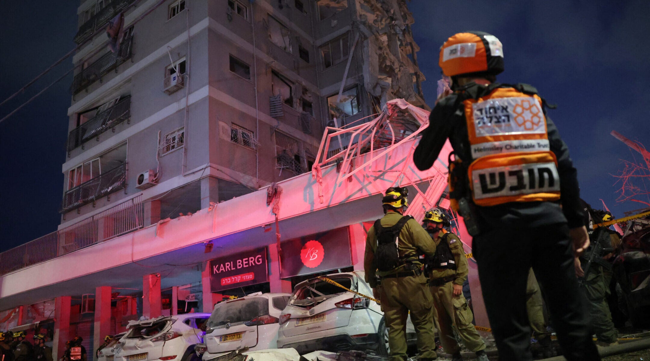 Responders work beside a damaged building following a strike by an Iranian missile in the Israeli city of Bat Yam, south of Tel Aviv, early on June 15, 2025.